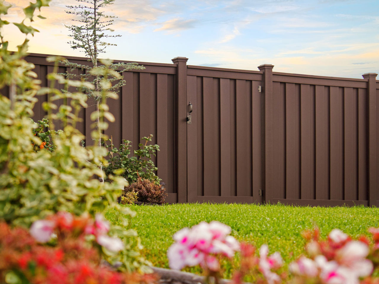 Beautiful brown Trex fence with a lawn and garden. 