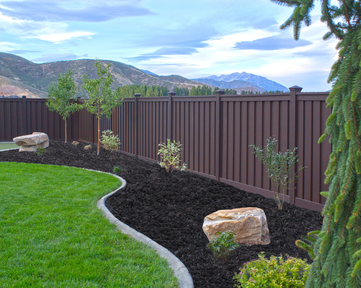 Beautiful brown Trex fence with a lawn and garden. 